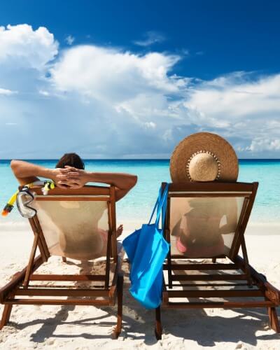 Couple relaxing on sun loungers by a clear blue sea on a sunny holiday