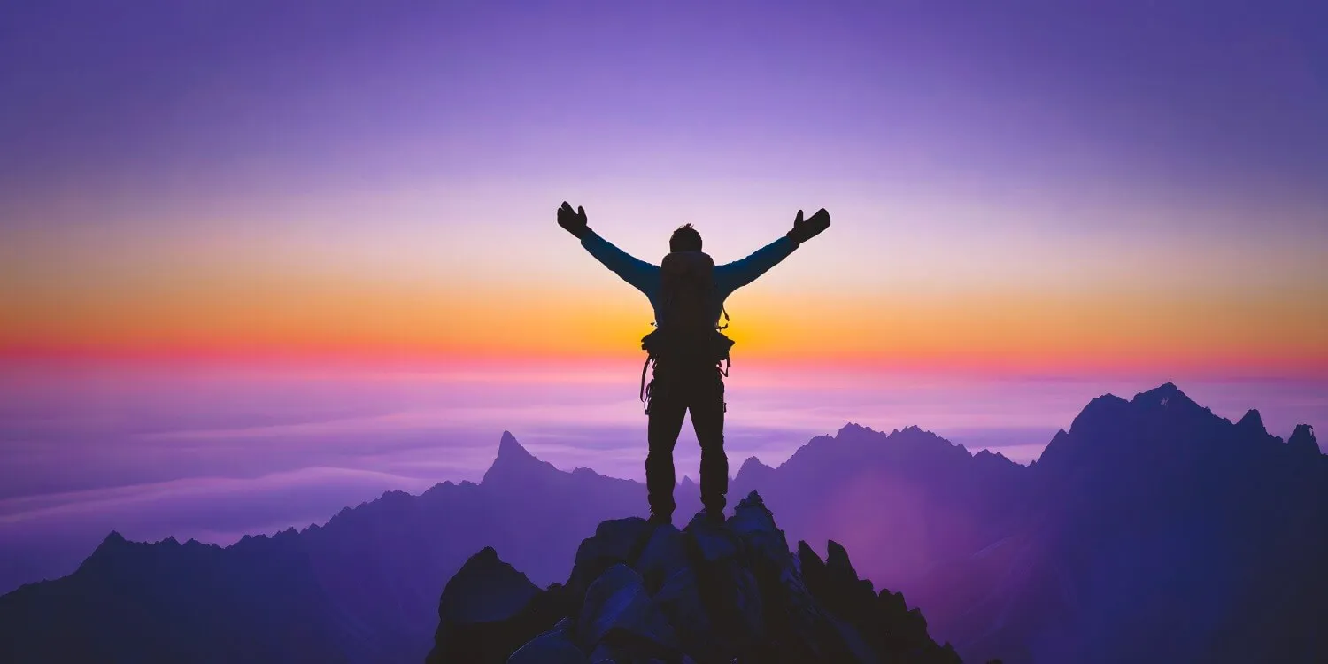 A hiker standing on a mountain summit at sunrise with arms raised